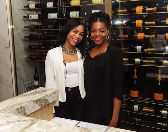 two women standing in front of a glass enclosed wine selection in moxies