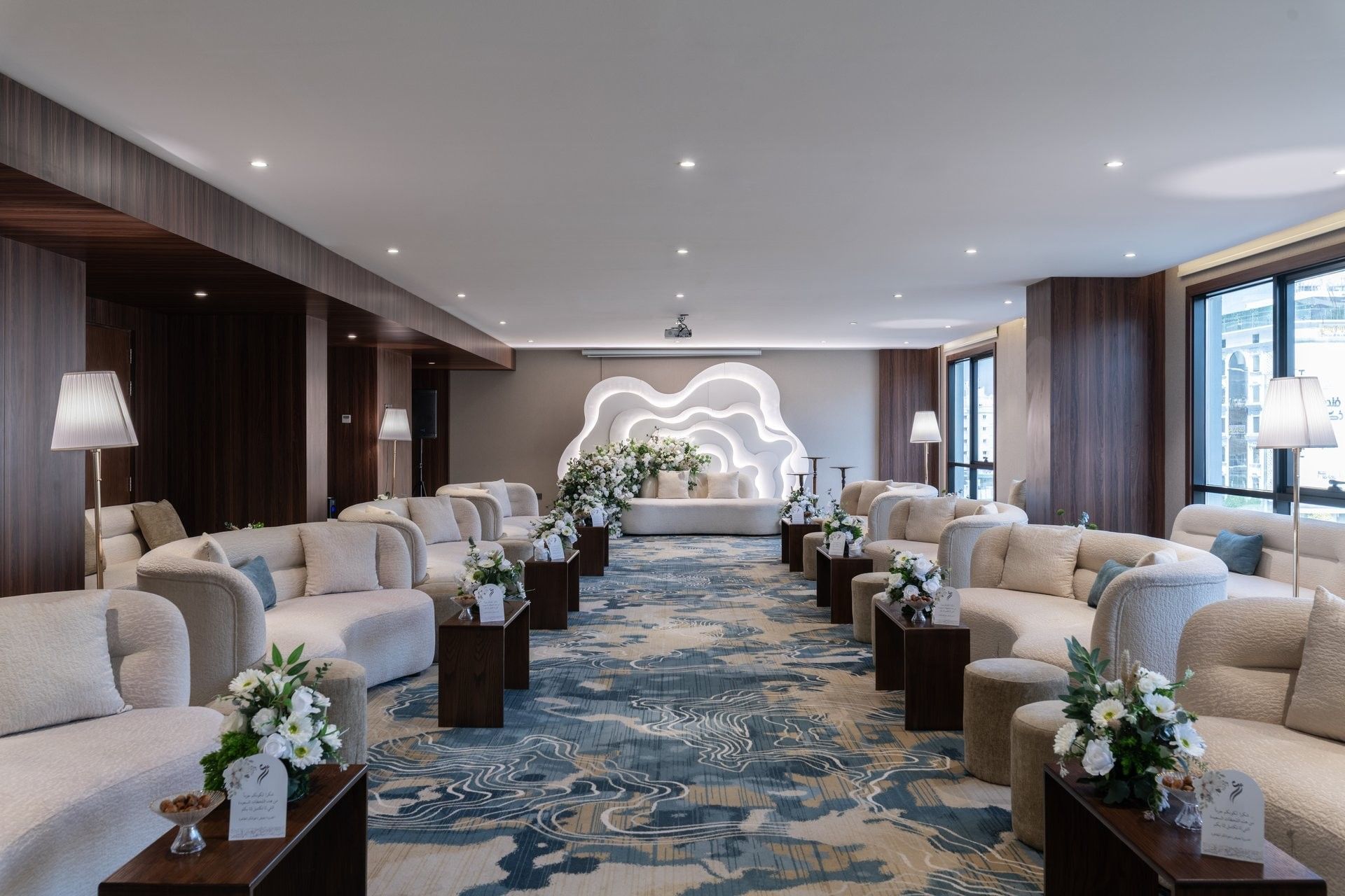 Cream sofas surrounding flower arrangements on a blue rug under bright lights in Amarige Hall at Warwick Hotels and Resorts