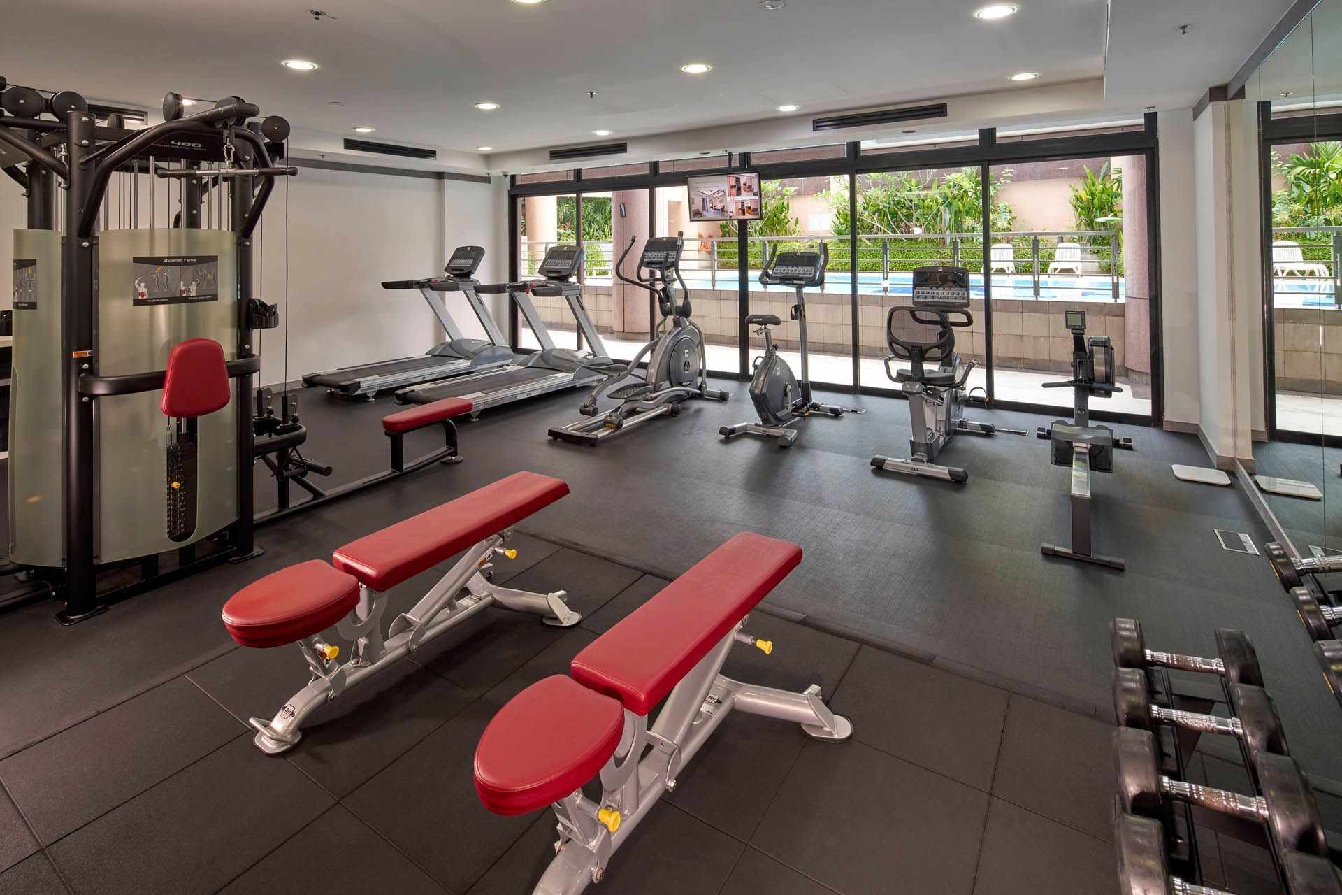 Modern gym with exercise machines, weight benches, and large windows overlooking the pool at Orchard Grand Court