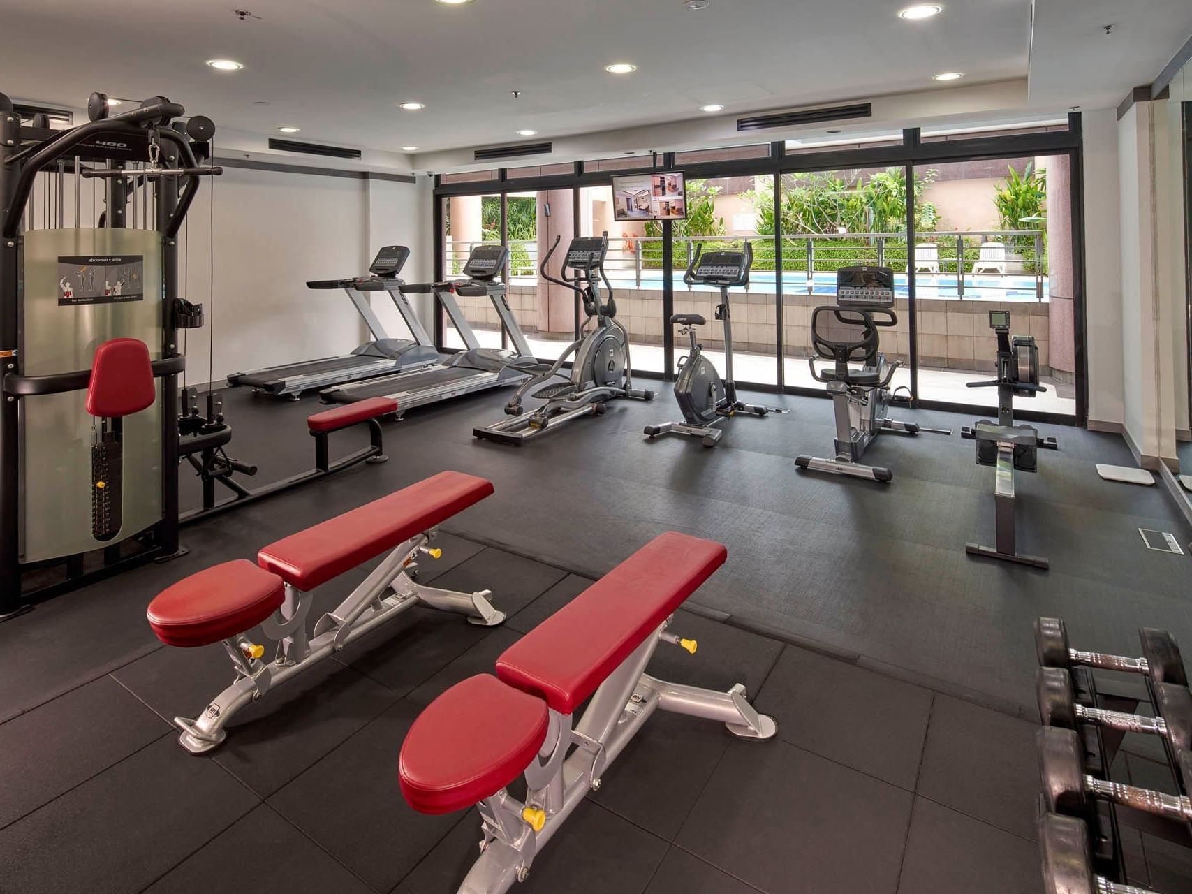 Modern gym with exercise machines, weight benches, and large windows overlooking the pool at Orchard Grand Court