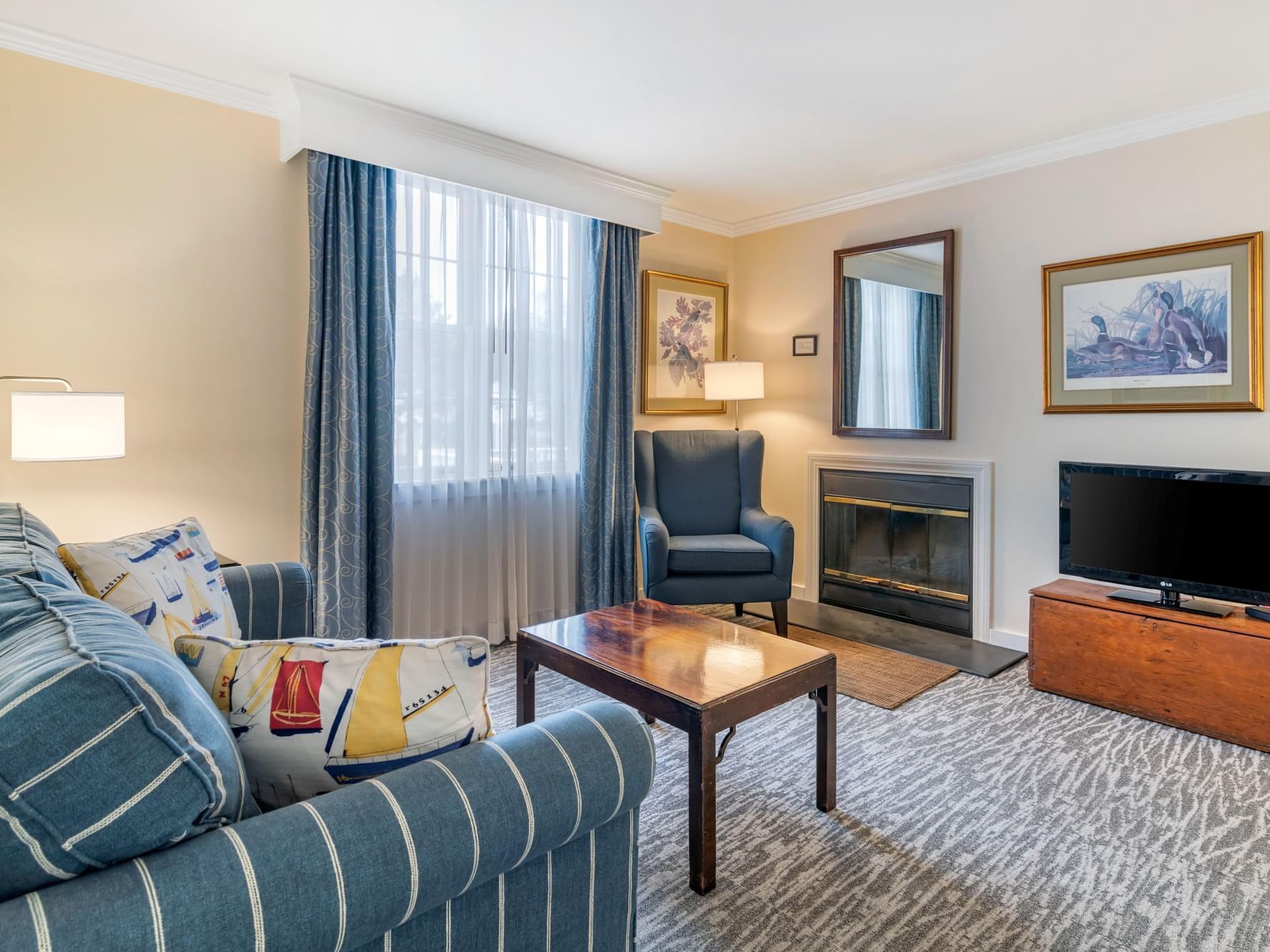 Cozy living area with blue couches, coffee table & TV stand in Queen 2 Room Suite at Harraseeket Inn
