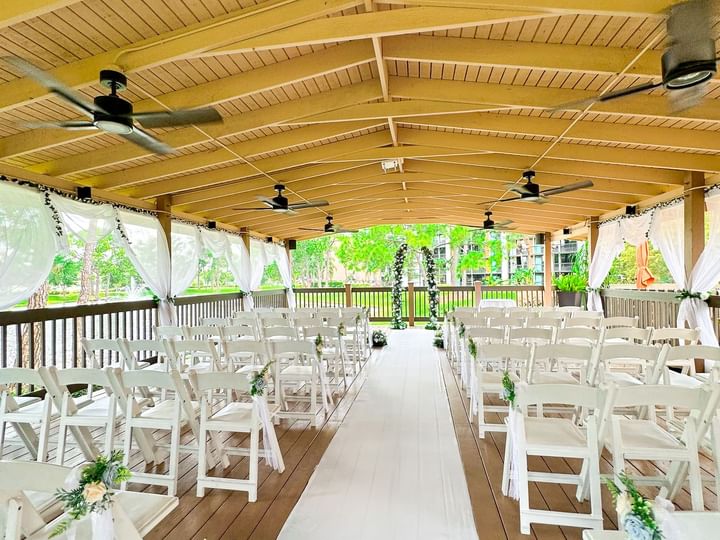 A beautifully decorated outdoor wedding venue with white chairs, aisle runner, and curtains.