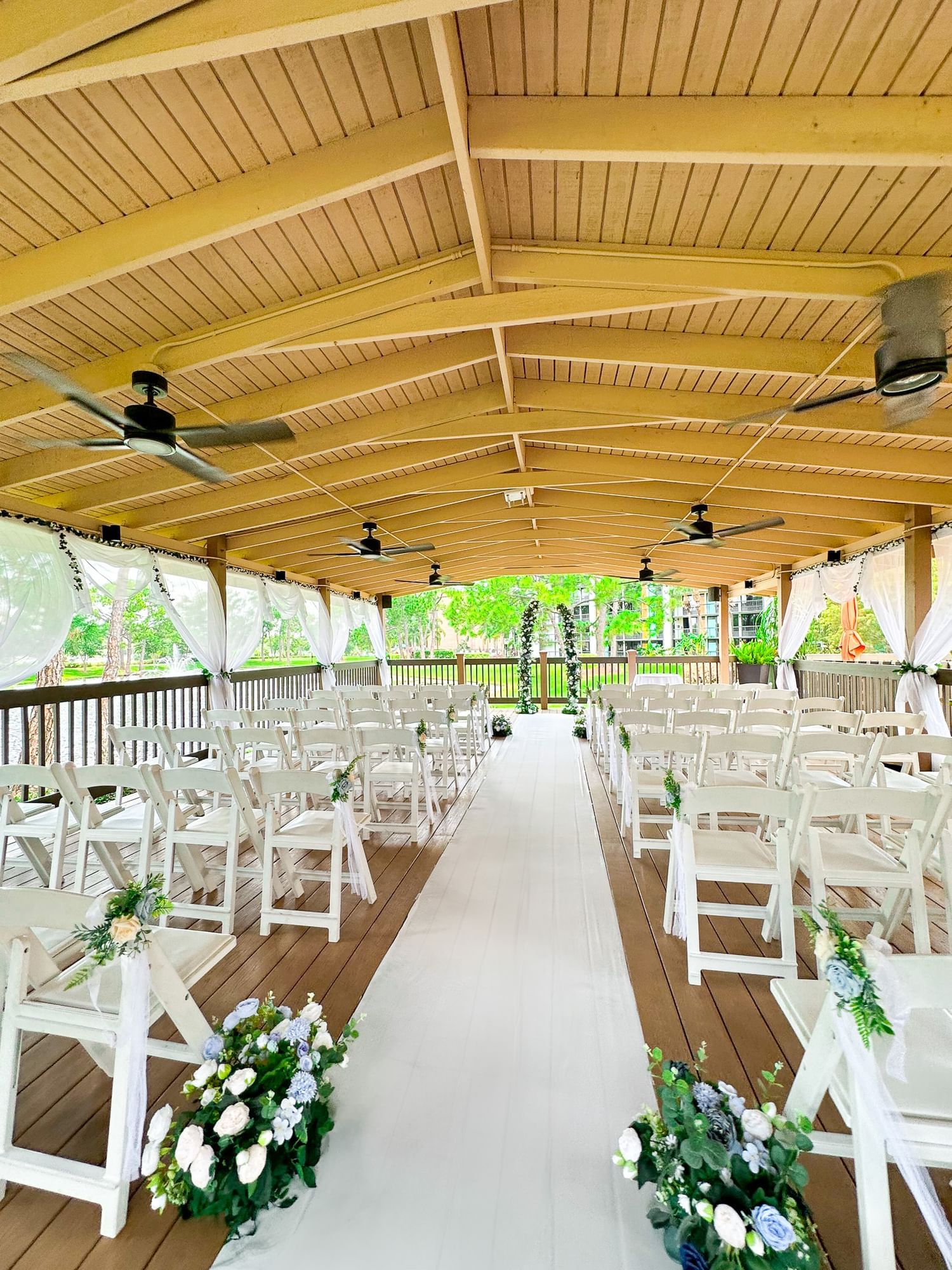 A beautifully decorated outdoor wedding venue with white chairs, aisle runner, and curtains.