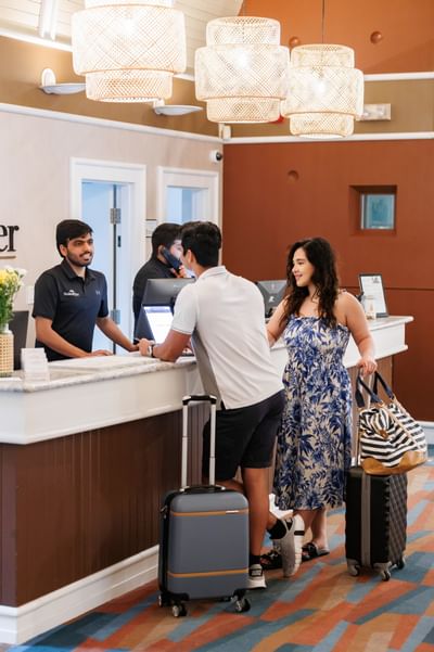 Guests standing with luggage by a reception desk under modern woven light fixtures at Rodd Brudenell River Resort