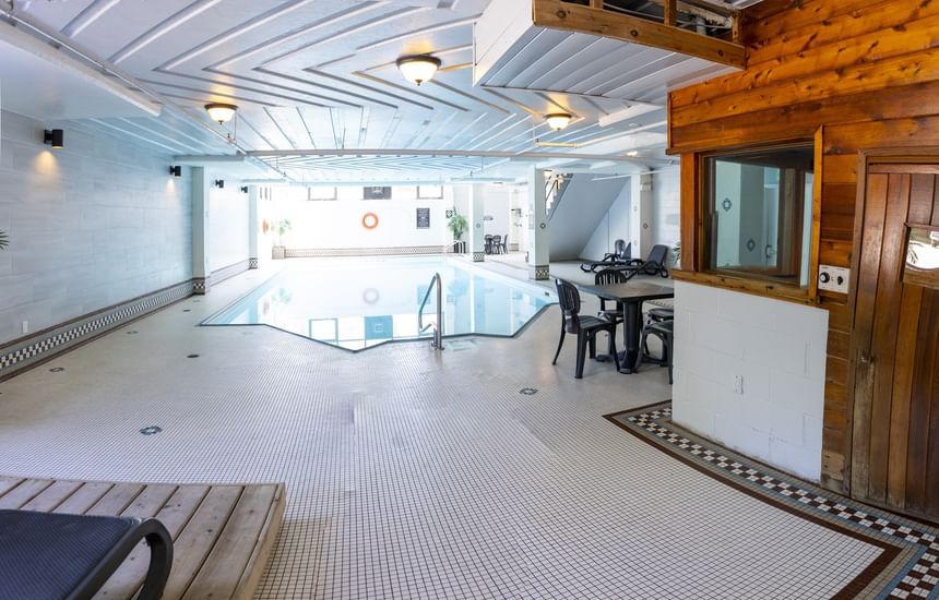 Indoor pool deck with a tiled floor, dining tables, lounge chairs, and a wooden sauna at Rodd Grand Yarmouth