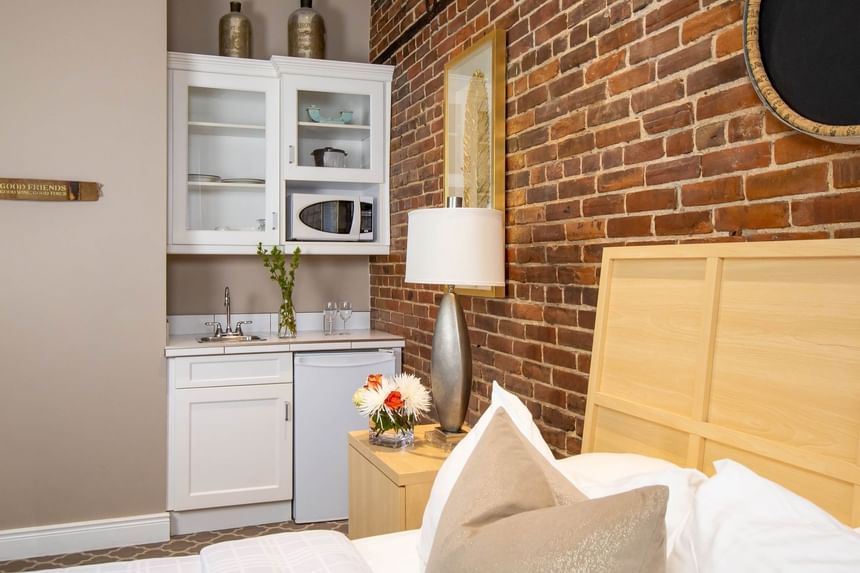 Queen bed, kitchenette, bedside cupboard with lamp & brick wall in Queen Premiere Chardonnay at Retro Suites Hotel