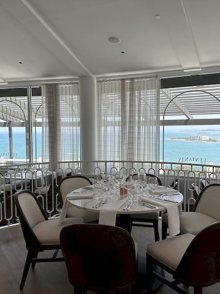 Ventanas Restaurant with a round table set, and large windows showcasing a scenic ocean view at El Conquistador Resort