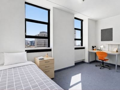 A neat hotel room with bed, desk, chair, and two windows at UniLodge Stafford House.