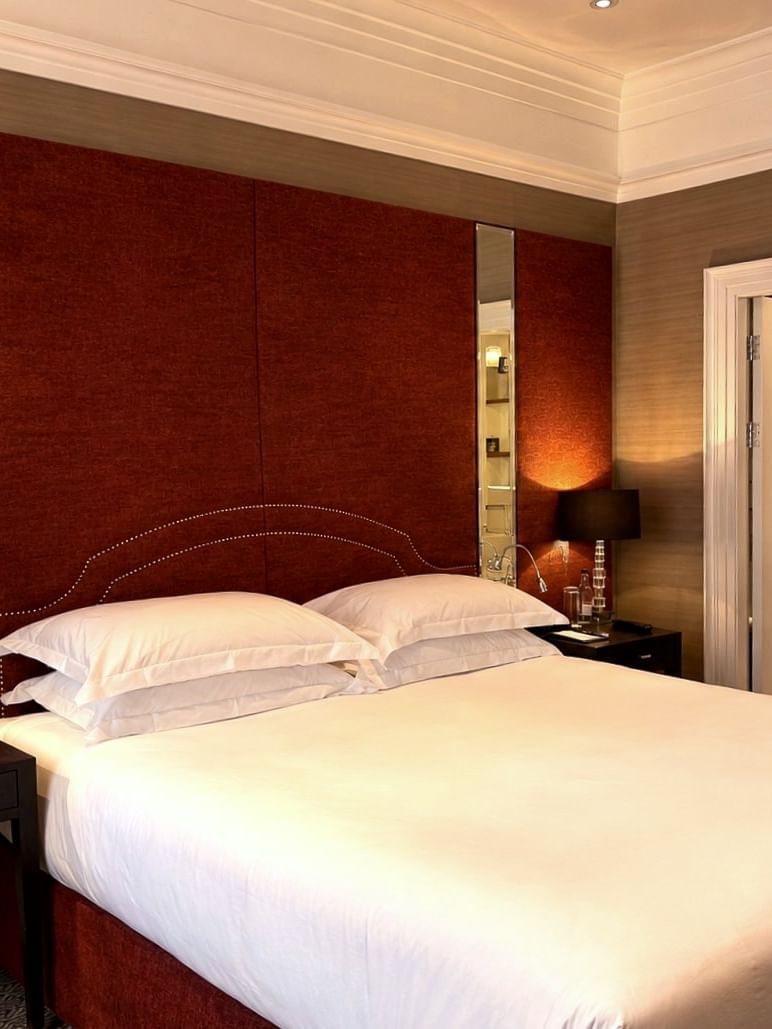 Large bed by mirrors under a red fabric headboard near an open door to a marble bathroom at Warwick Hotels & Resorts