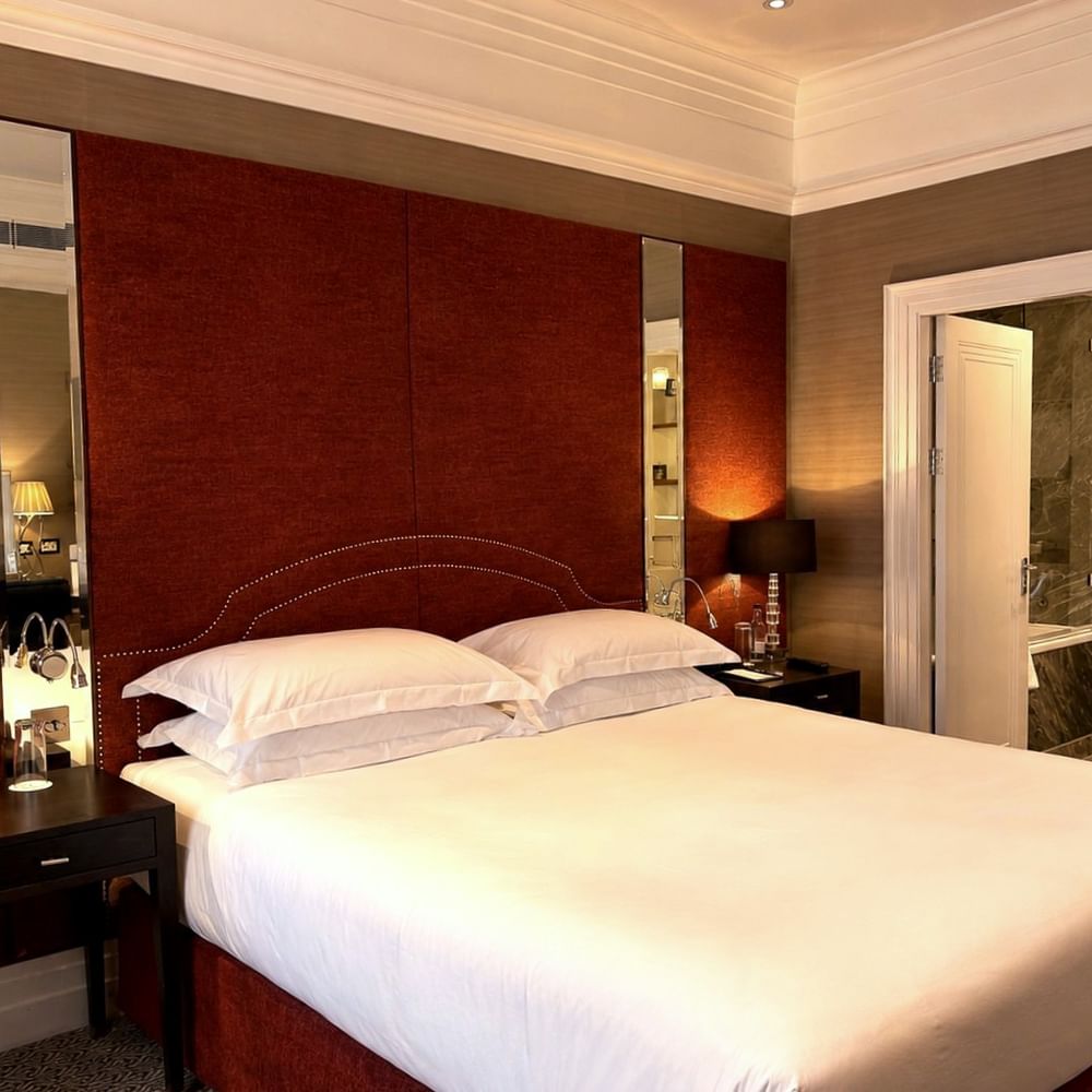 Large bed by mirrors under a red fabric headboard near an open door to a marble bathroom at Warwick Hotels & Resorts