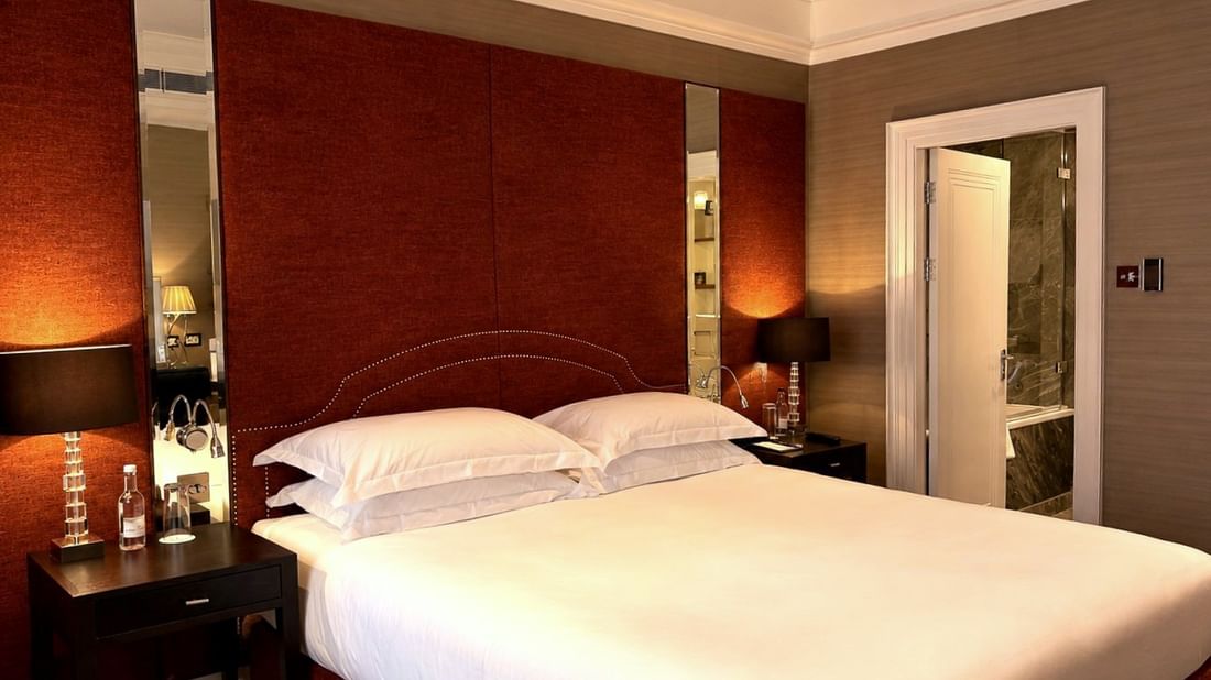 Large bed by mirrors under a red fabric headboard near an open door to a marble bathroom at Warwick Hotels & Resorts