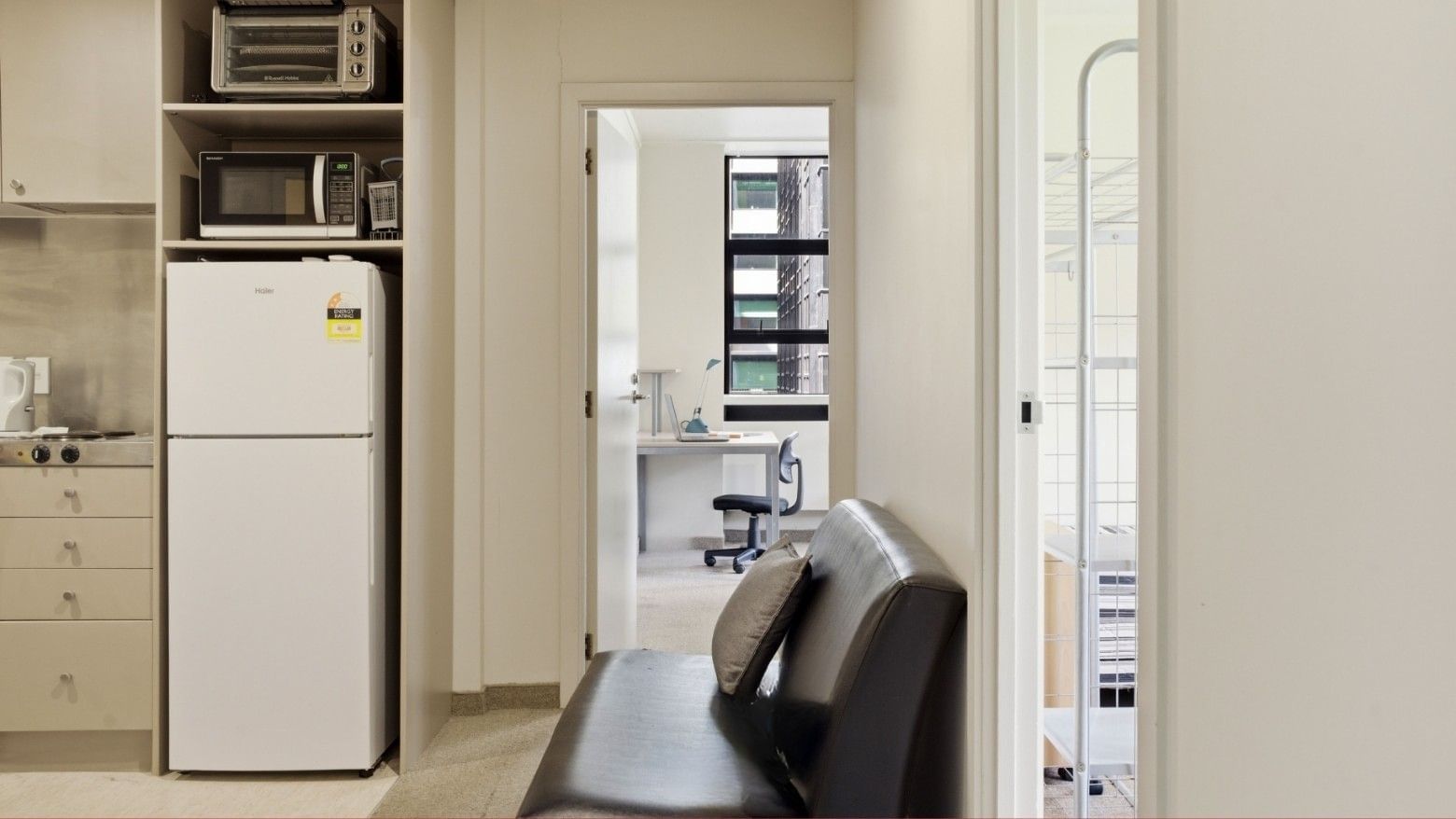 Living room with black leather sofa and white refrigerator at UniLodge Stafford House.