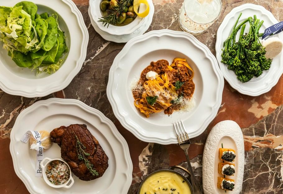 Elegant dining spread at Remi in Granduca Houston featuring steak, pasta, fresh salad, and seasonal vegetables