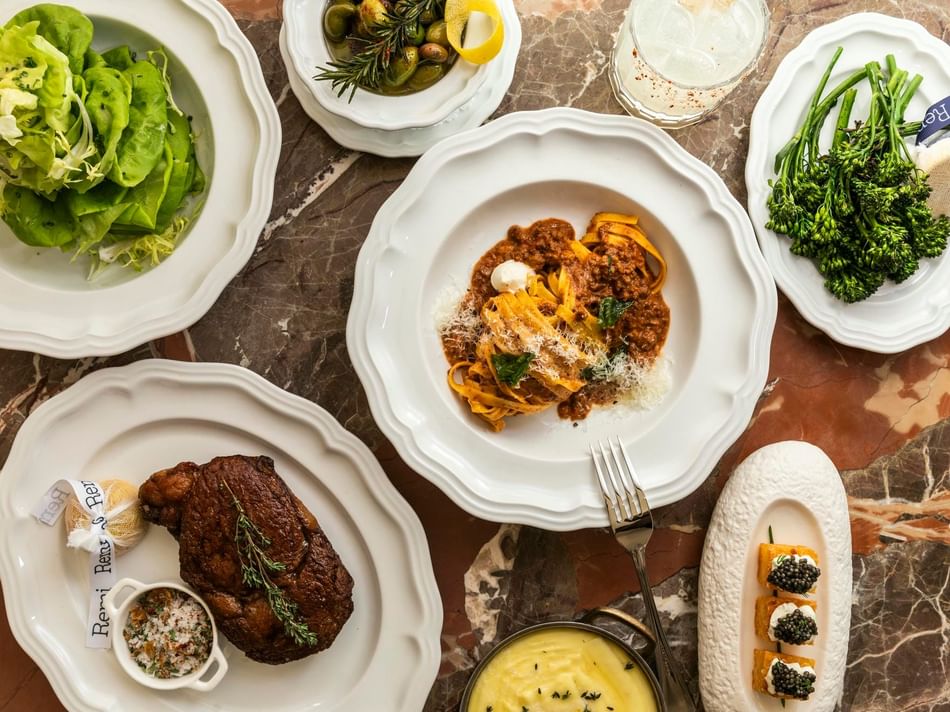 Elegant dining spread at Bar Remi in Granduca Houston featuring steak, pasta, fresh salad, and seasonal vegetables