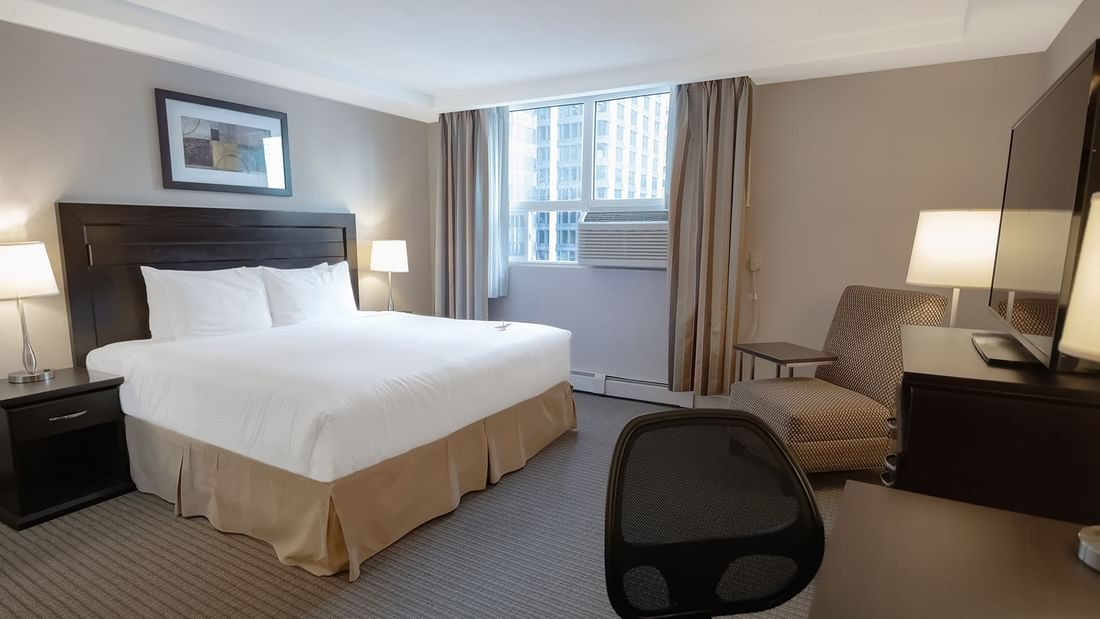 Hotel room with bed, TV, work desk, chair, rest chair, nightstand, and window