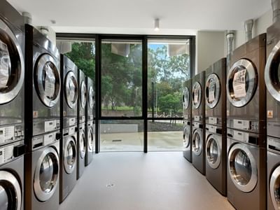 Row of washing machines and dryers in a clean, modern laundry room.