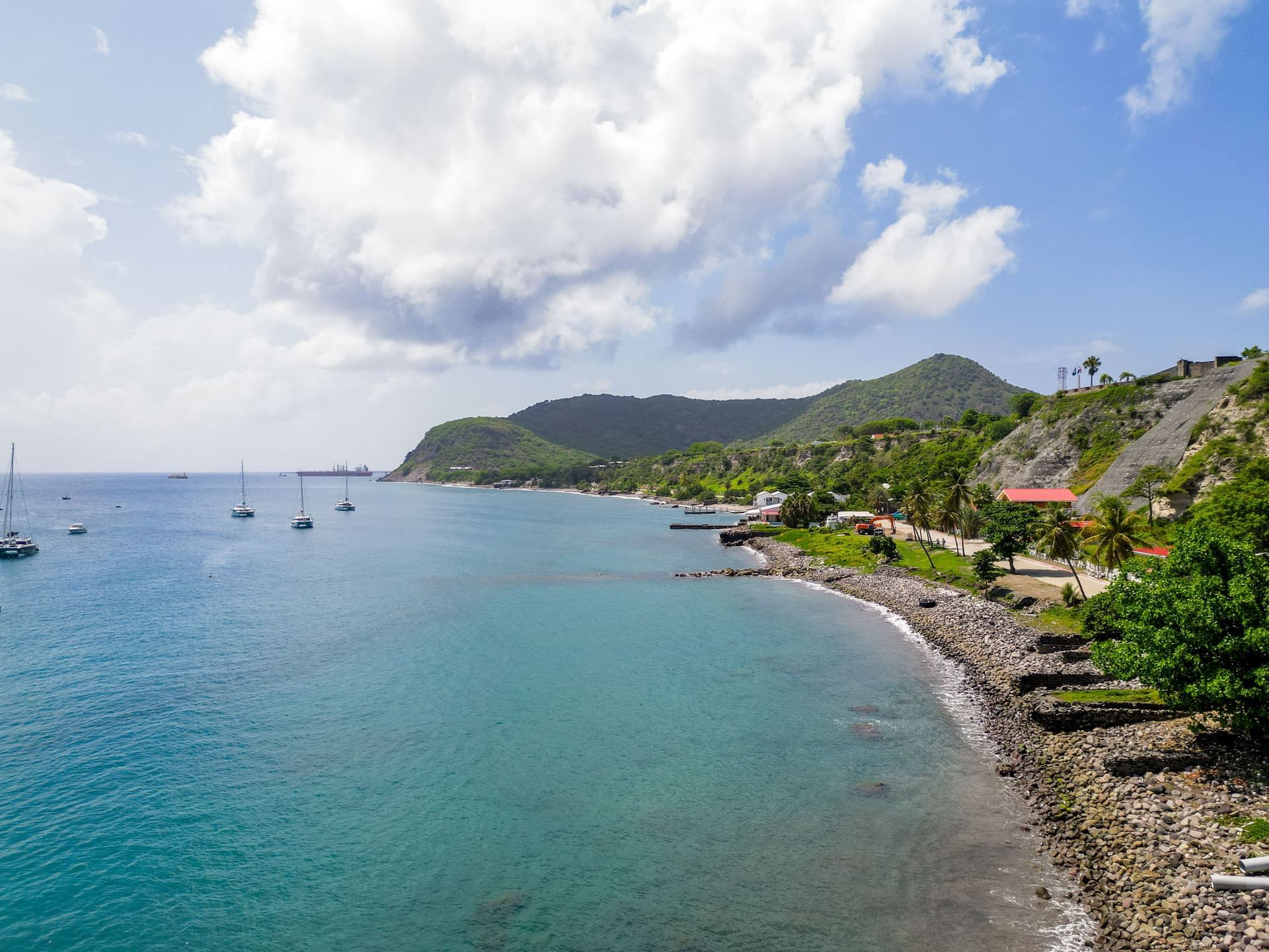 Coastal view with sailboats in calm blue waters, lush hills, and a scenic shoreline with trees near Golden Rock Resort