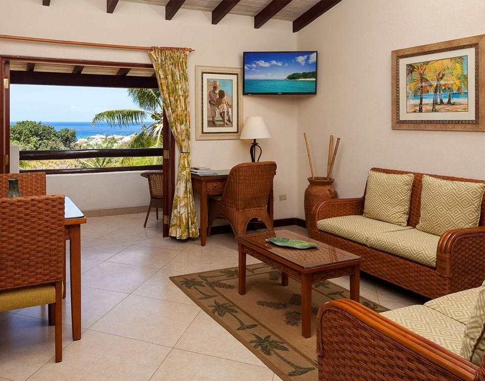 Dining table & wicker sofa by open terrace doors with scenic ocean view in Ocean View Suite at Sugar Cane Club Hotel & Spa