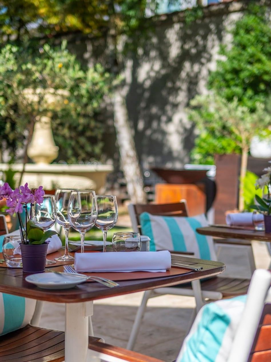 Set tables with wine glasses and purple flowers on an outdoor terrace at Hotel Barsey by Warwick