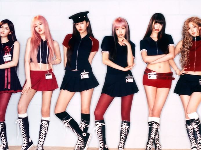 Six women in matching outfits posing for the camera in front of a white wall.