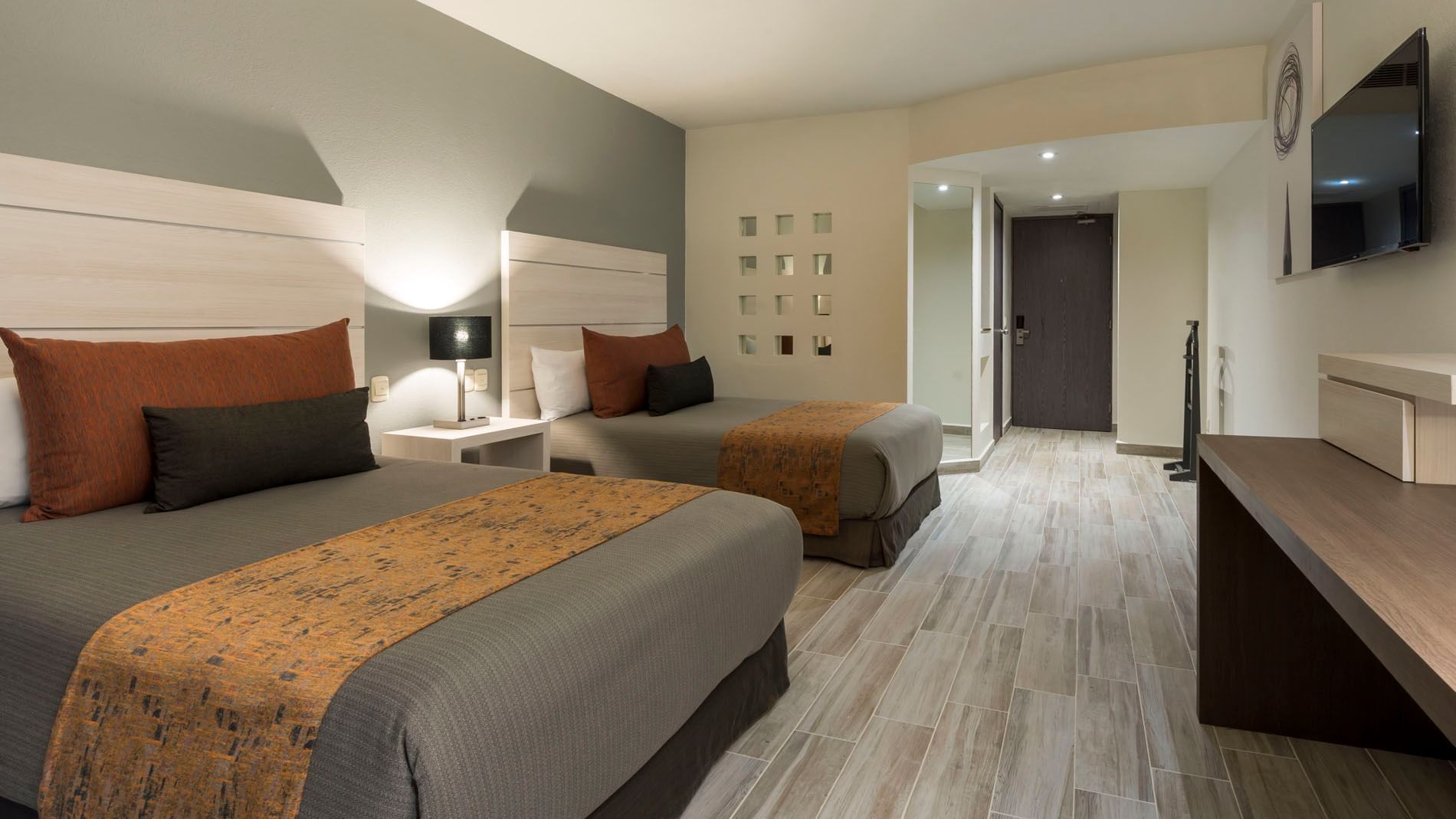 Deluxe Two Double Room with white headboards, a bedside lamp, and wooden floor tiles at Real Inn San Luis Potosi