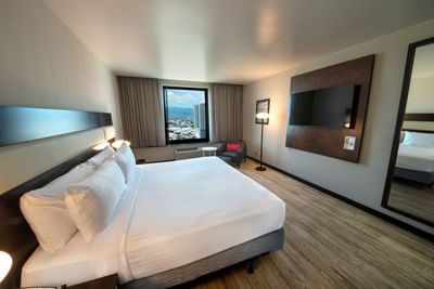 Room with large bed, TV, seating area, and a view of the city through windows at D Sabana Hotel, San Jose Costa Rica Hotel