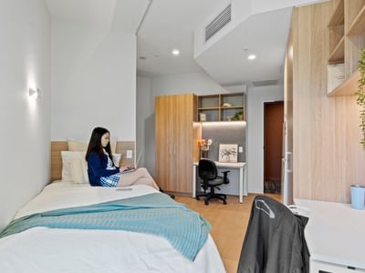Woman working on laptop on bed in UniLodge Brisbane City student room.