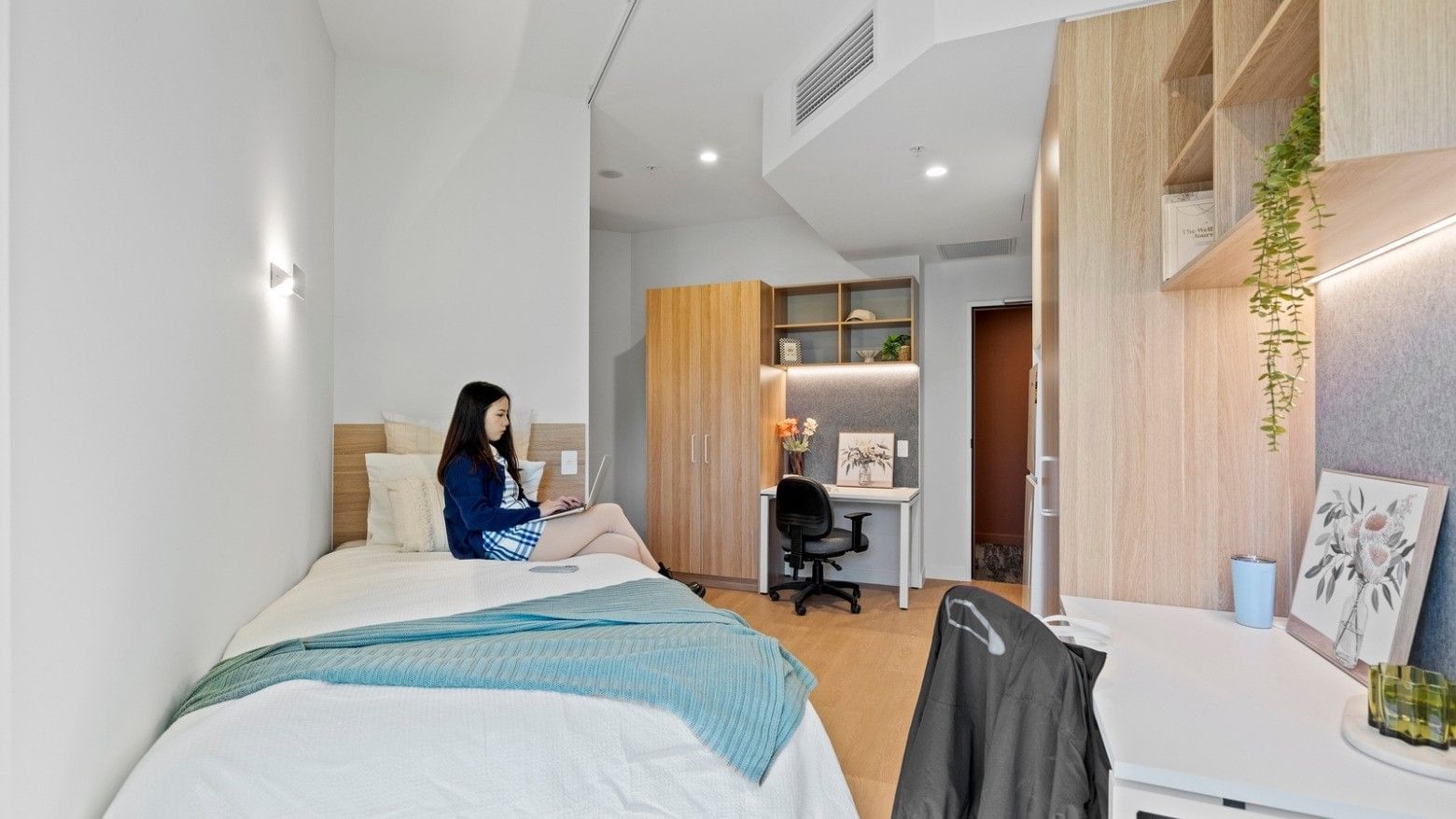 Woman working on laptop on bed in UniLodge Brisbane City student room.