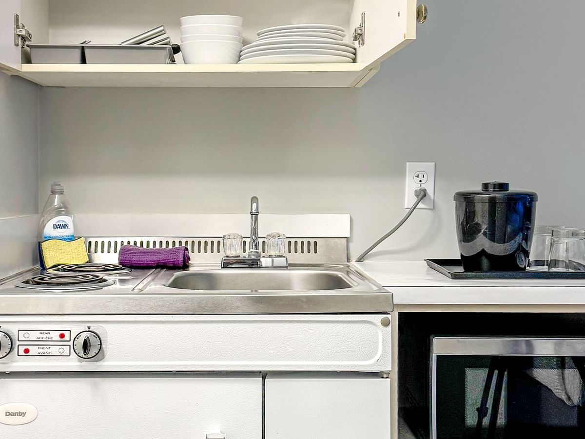 Hotel guestroom kitchenette with sink, microwave, stove and dishes