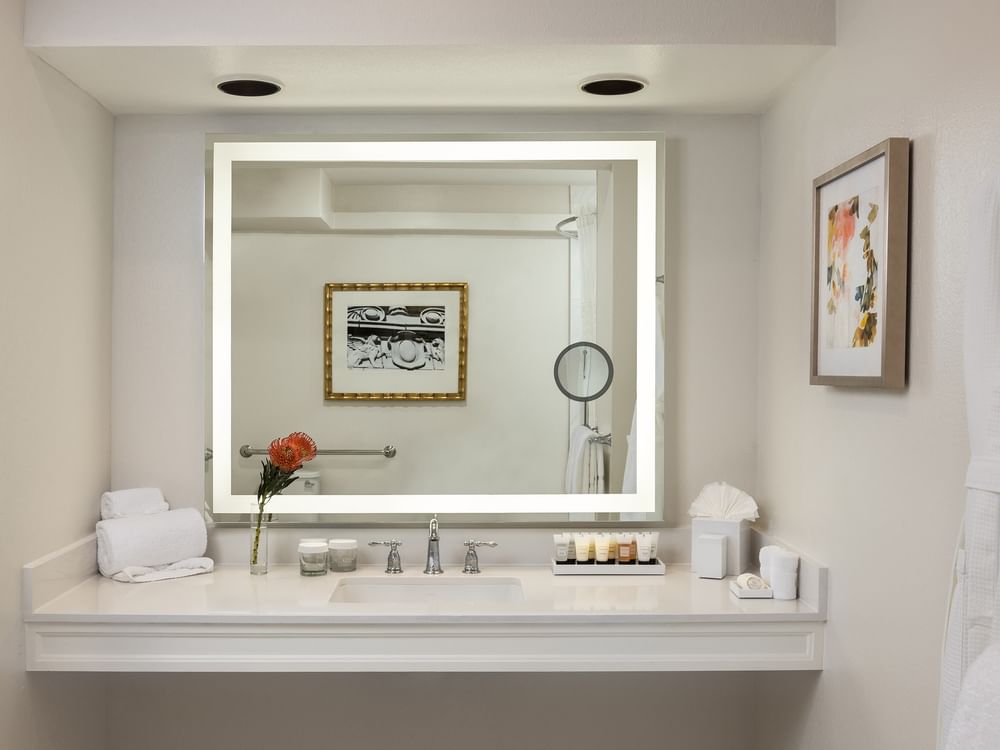 Large lighted mirror with toiletries under a recessed light in Deluxe Suite Accessible at Warwick Melrose Dallas