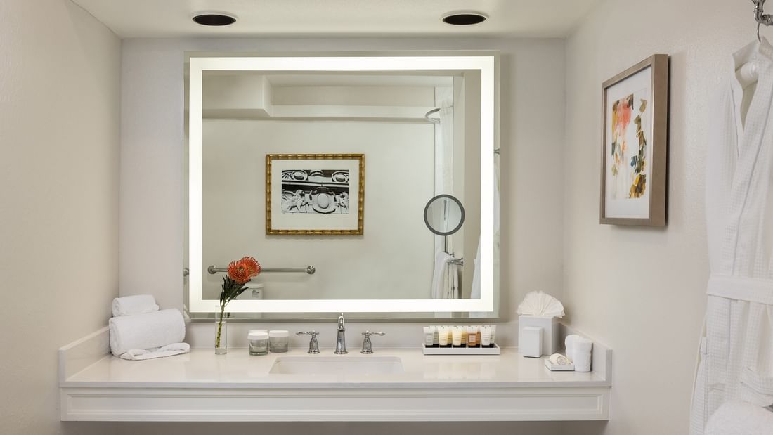 Large lighted mirror with toiletries under a recessed light in Deluxe King Accessible at Warwick Melrose Dallas