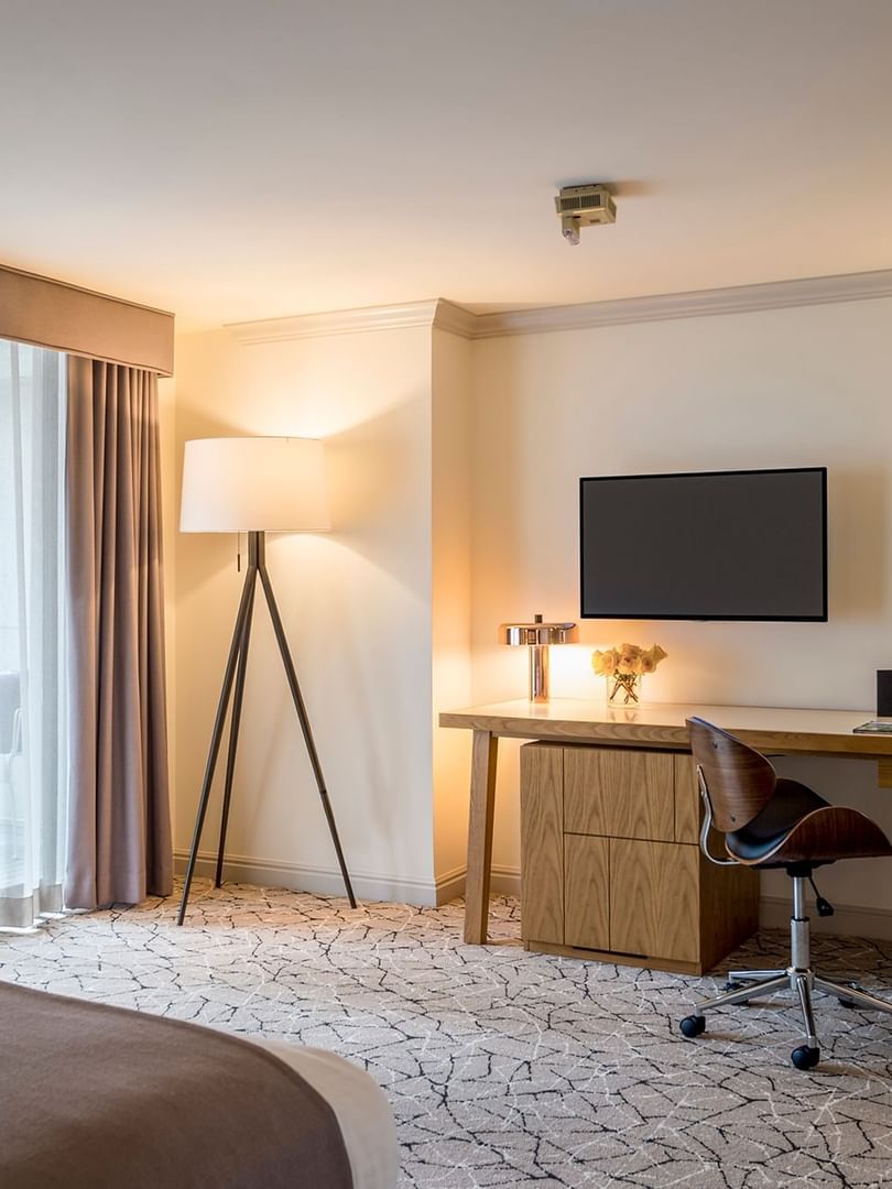 Wooden desk by a tripod lamp under a wall TV iin Accessible Classic Rooms featuring a patterned rug at Warwick Denver