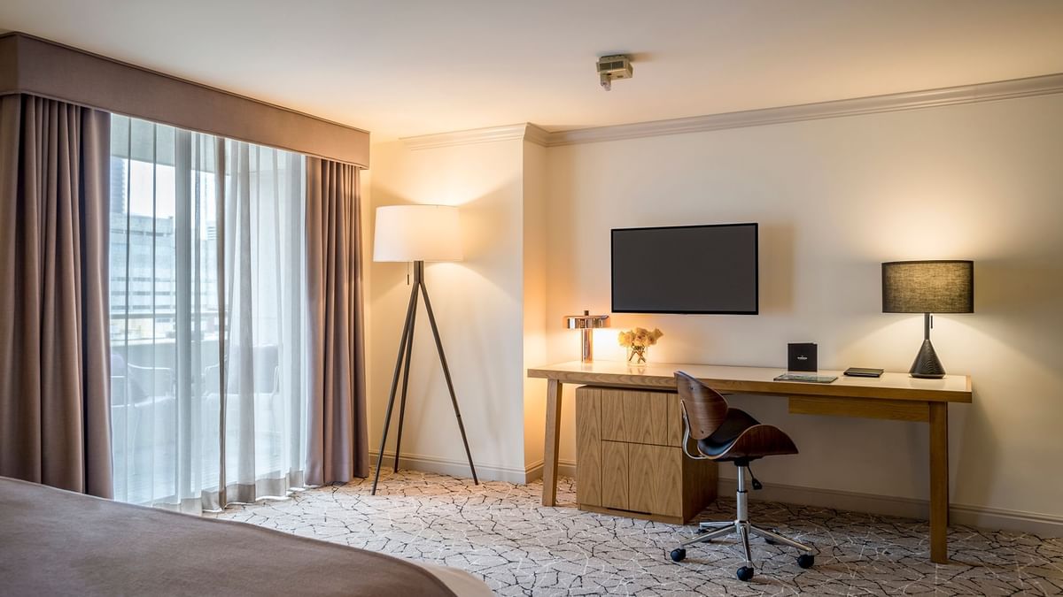 Wooden desk by a tripod lamp under a wall TV iin Accessible Classic Rooms featuring a patterned rug at Warwick Denver