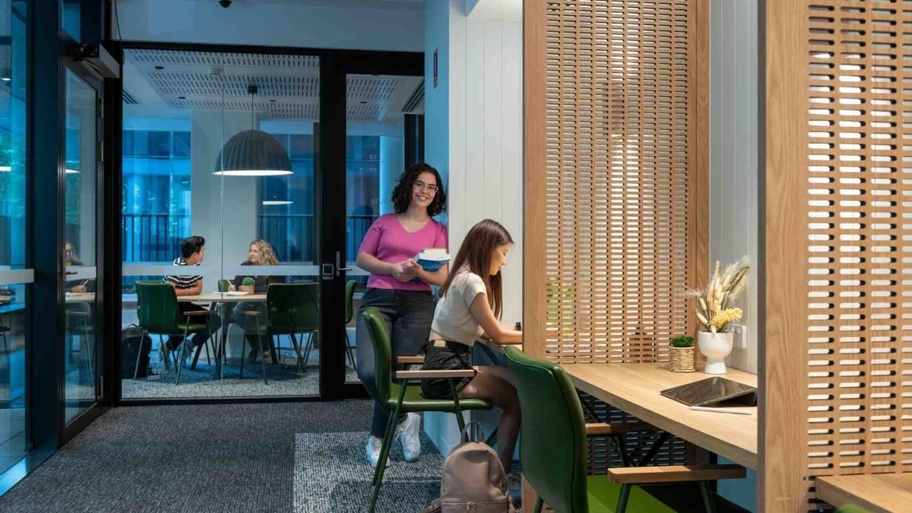 Residents at a study lounge, one standing and the other sitting at a desk.
