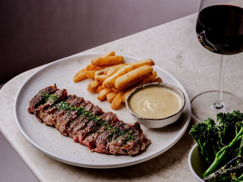 Steak, fries, sauce, and wine on a table at The May Fair Hotel, London.
