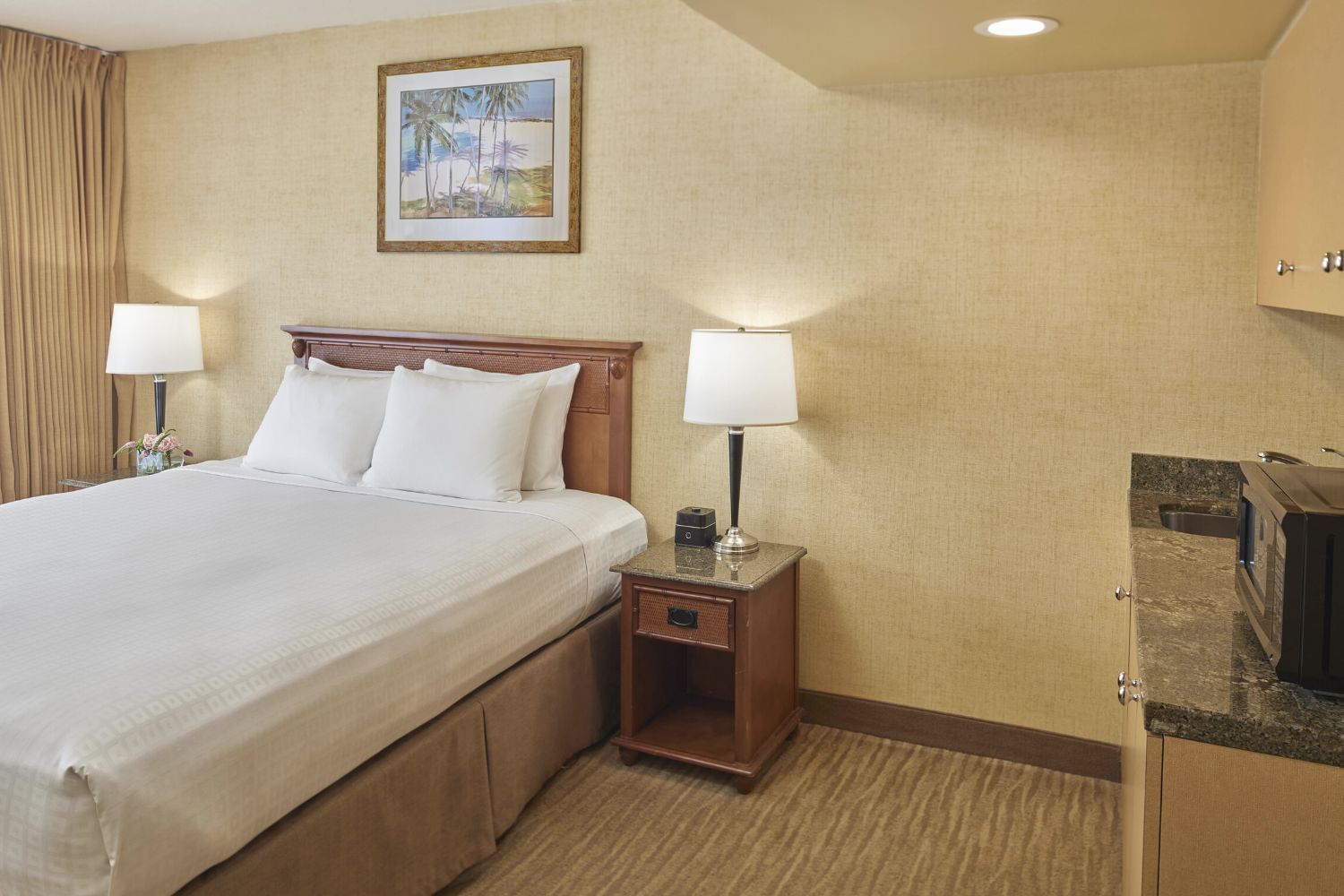 A hotel room with a bed, nightstand, lamps, and a painting on the wall.