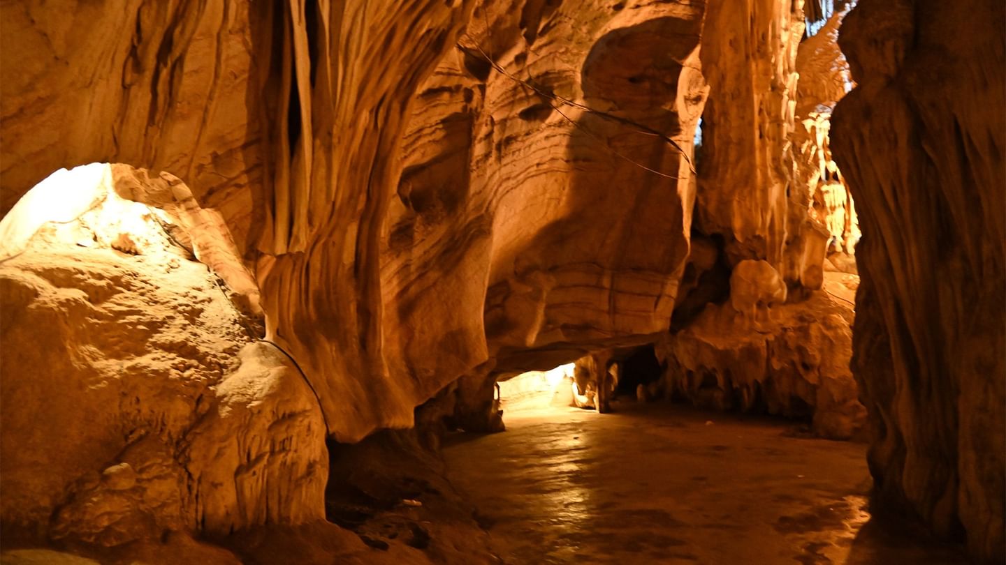 A cavern with rock formations, illuminated patches, and a narrow path leading into the cave.