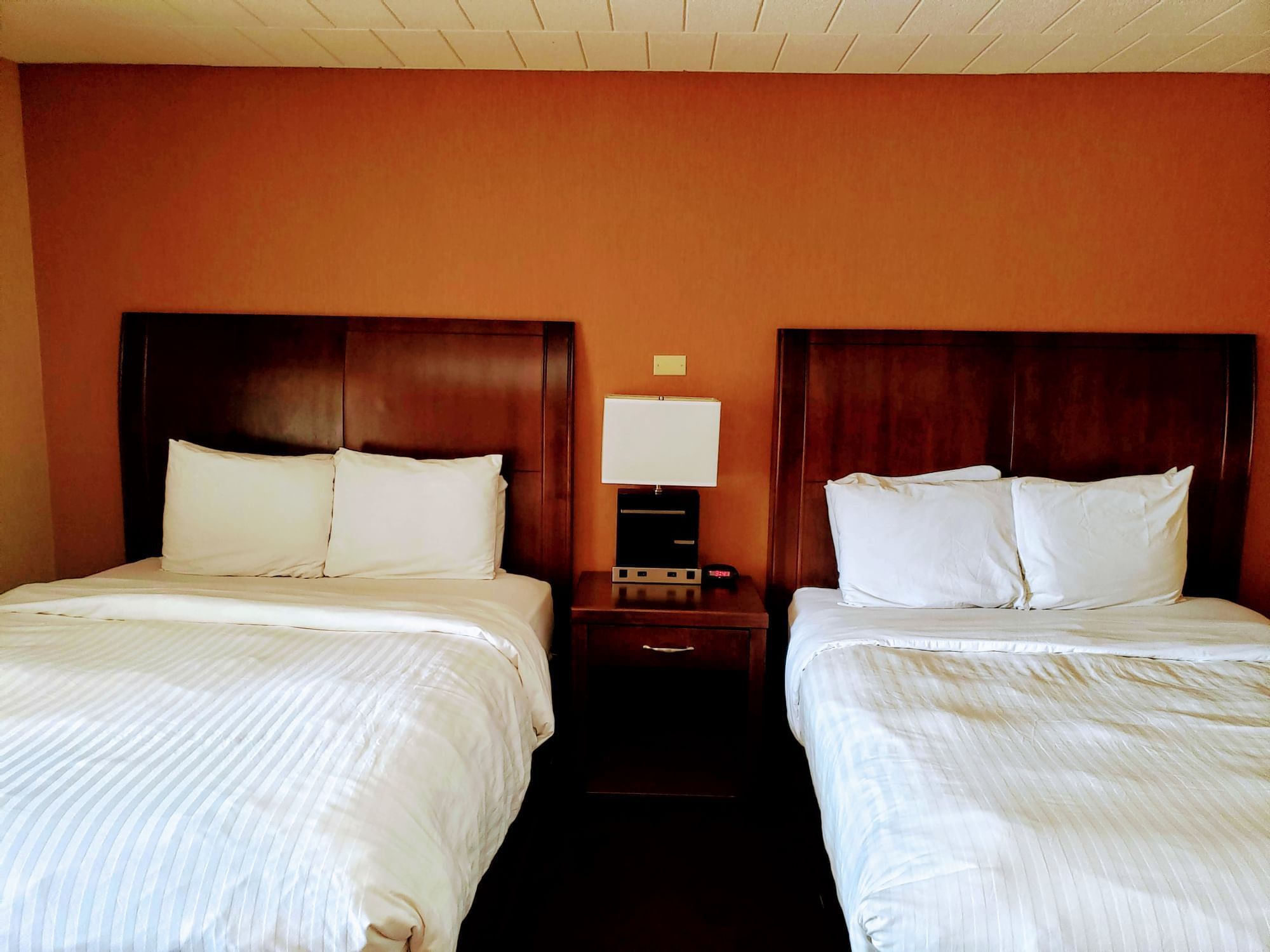 Two queen beds with white linens and a nightstand in between at Evergreen Resort in Cadillac.