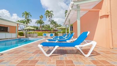 Rows of blue lounge chairs on a tiled patio beside a refreshing outdoor swimming pool at Worthing Court Apartment