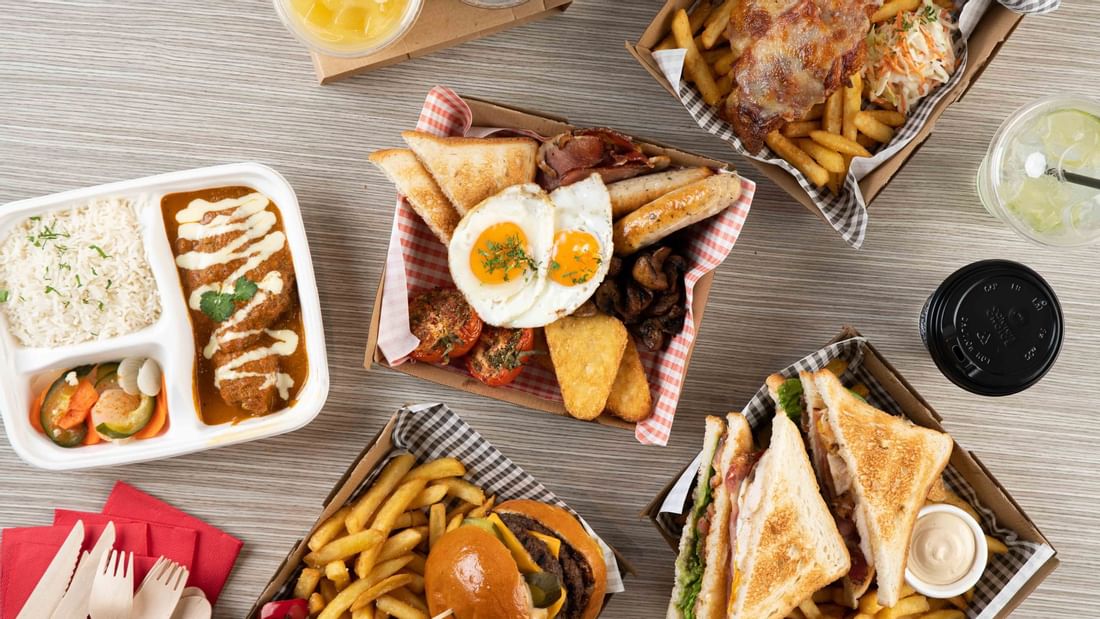 Delicious spread of burgers, curry with rice, fries, and drinks served on a table in Grab & Go at Ibis Adelaide