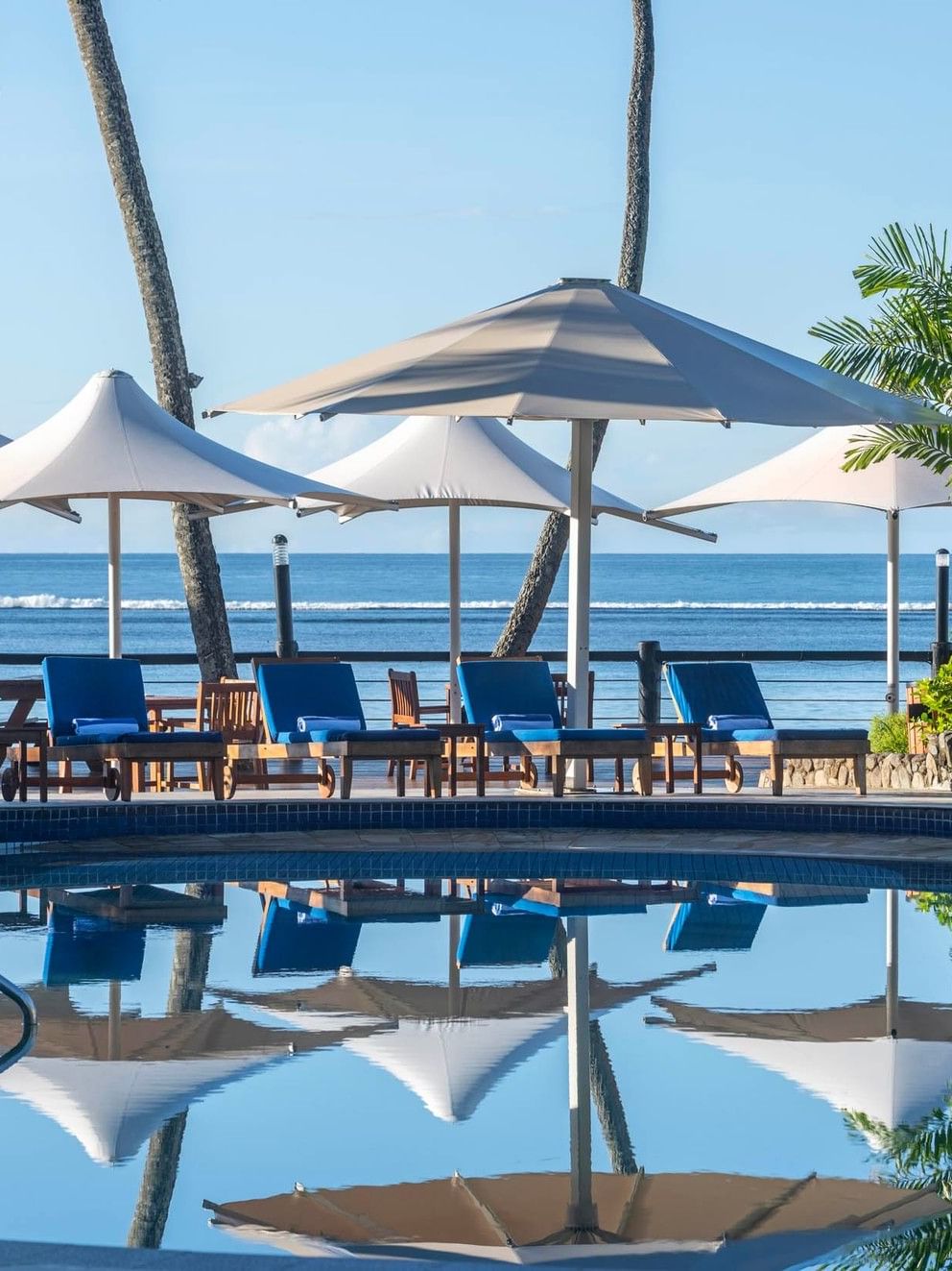 Beachfront swimming pool with blue lounge chairs and umbrellas at Warwick Fiji Resort and Spa, Korolevu.