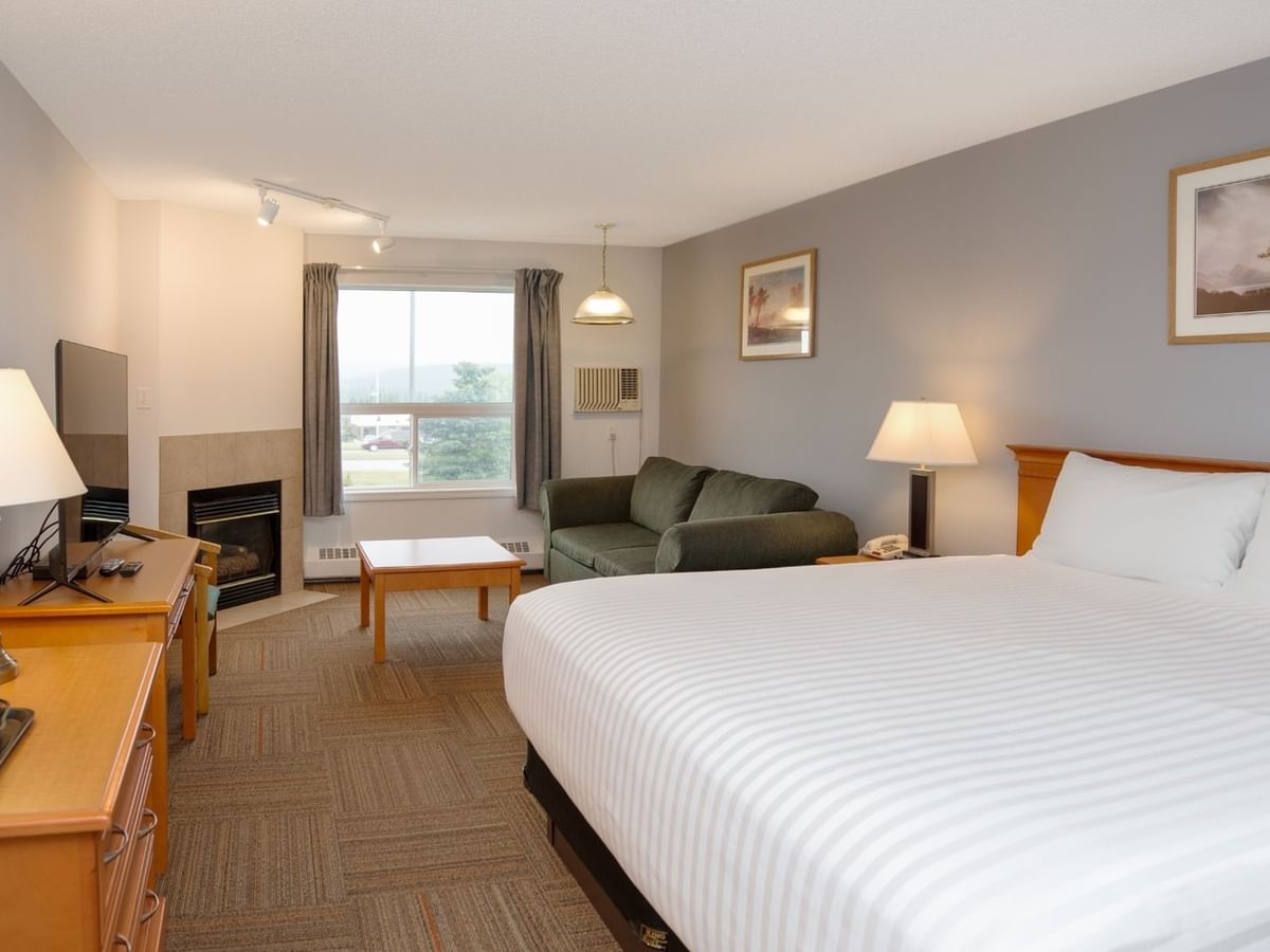 A hotel room with a large bed, green couch, desk, TV, fireplace, and two framed pictures on the wall.