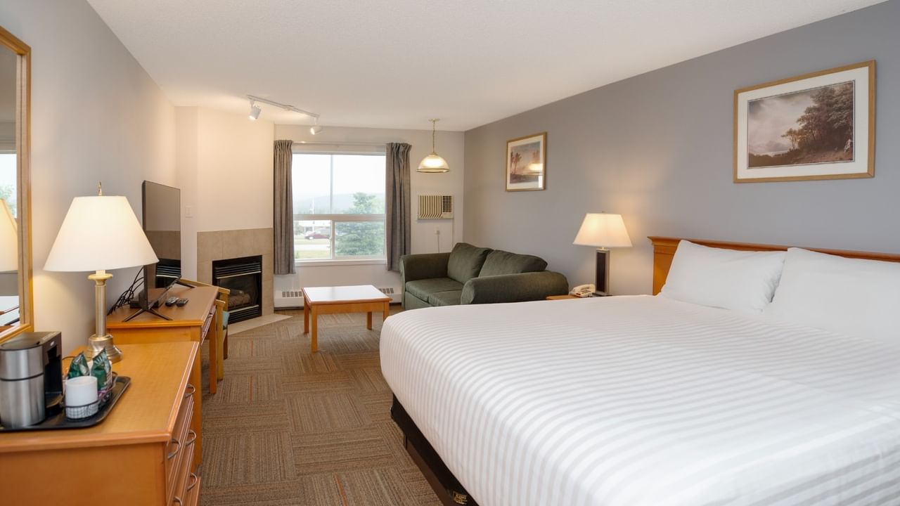 A hotel room with a large bed, green couch, desk, TV, fireplace, and two framed pictures on the wall.