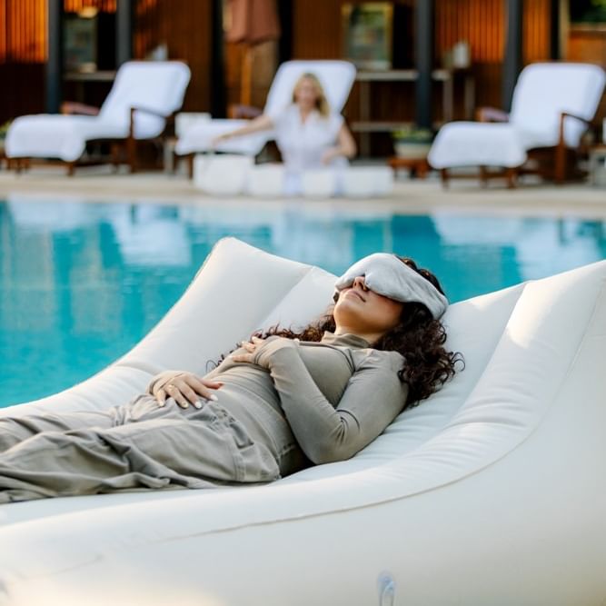 Woman relaxing on floating lounger in pool wearing eye mask during Summer Wellness Series: Sunset Floating Sound Bath