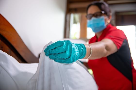 A woman in gloves and a mask cleaning a bed in room at Blackcomb Springs Suites