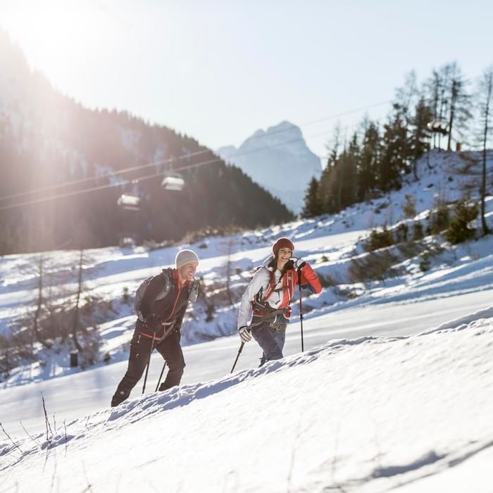 Two hikers with trekking poles ascending a snowy mountain trail near Falkensteiner Residences Edelweiss