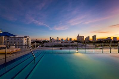 Rooftop Pool with a railing and a city in the background from the Fairwind Hotel Miami in the evening