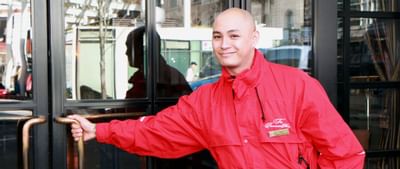 Welcoming hotel staff member in a red jacket holds the door open from the outside of Paramount Hotel Portland