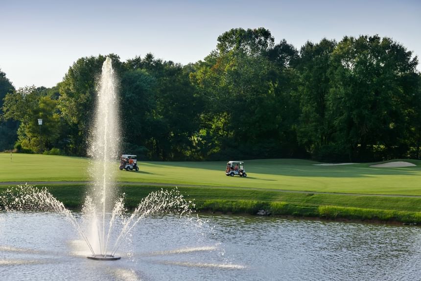 Golf course fountain spraying water beside two carts on the grassy fairway at Clemson University Conference Center & Inn