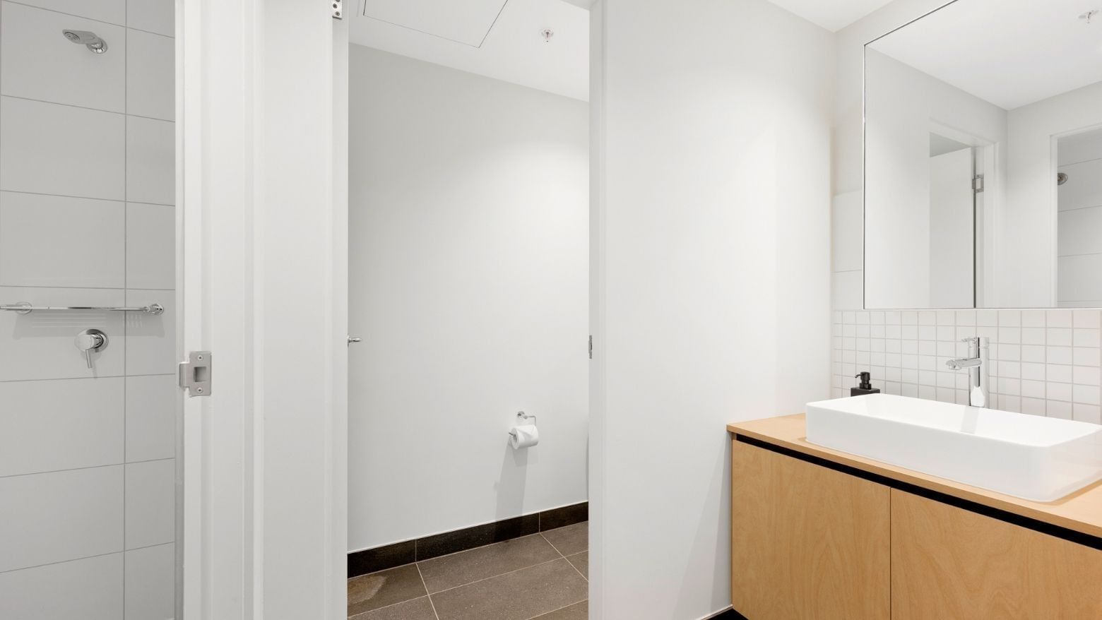 Clean bathroom with white sink, mirror, and wooden cabinet in La Trobe University apartments.